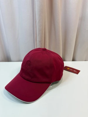 Loro Piana - Snygg vinröd keps från Loro Piana med broderad logga framtill. Klassisk böjd skärm med vit kant och justerbar rem bak. Tillverkad i ett lätt och slitstarkt material som passar perfekt till streetwear eller sportig stil.