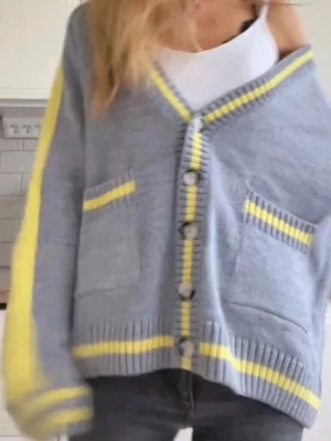 Grå kofta med gula detaljer - Snygg grå kofta med knappar framtill och gula samt vita ränder längs kanterna och på fickorna. Koftan har två framfickor och ribbstickade muddar. Perfekt för dig som gillar en avslappnad men trendig stil.