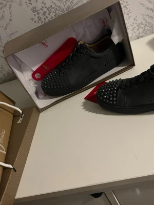 Gråa Louboutin sneakers med nitar - Säljer ett par gråa sneakers från Christian Louboutin med mattsvarta nitar på tån och klassisk röd sula. Skorna har lågt skaft, snörning och är tillverkade i läder. Grymt statement-plagg för dig som vill sticka ut.