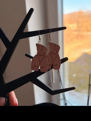 Bruna örhängen i kroppform - Handgjorda örhängen i form av en kropp, tillverkade i brun plast med svarta linjer som markerar detaljer. Hängande modell med metallkrok. Perfekt för dig som gillar statement-smycken och vill sticka ut.