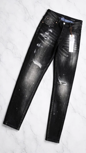 Svarta jeans med slitningar (purple jeans) - Säljer ett par svarta jeans med distressed detaljer och vita färgstänk. Jeansen har smal passform och klassisk femficksdesign. Perfekta för en edgy och trendig look. Tveka inte att skicka iväg ett meddelande vid funderingar eller om du vill ha fler bilder, priset kan diskuteras vid snabb affär.