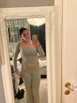 Grått tvådelat set med lång ärm - Säljer ett trendigt grått tvådelat set med en axelbandslös topp och matchande långärmad bolero samt byxor med mid midja. Setet är i mjukt stretchigt material och har en slim fit passform som framhäver figuren.