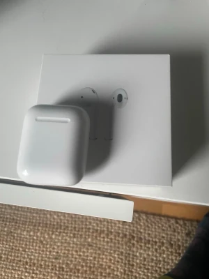 Apple AirPods med laddningsetui - Säljer ett par trådlösa Apple AirPods med vitt laddningsetui. Snygg och stilren design i blank plast, perfekt för dig som vill ha smidiga hörlurar till mobilen. Kommer i originalförpackning och laddas enkelt i det medföljande laddar. Hör av om du har frågor knappt använda par ett par få gånger 