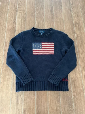 Mörkblå stickad USA tröja Polo Ralph Lauren - Mörkblå stickad tröja från Polo Ralph Lauren med amerikansk flagga broderad på bröstet. Tröjan har rund halsringning, ribbstickade muddar och nederkant samt RL-broderi vid fållen. Perfekt för dig som gillar klassisk preppy stil. Storlek 164! Skriv till mig vid intresse eller frågor! MVH 🤗