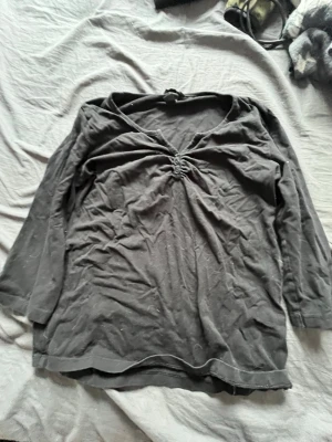 Svart v-ringad topp från H&M - Svart topp från H&M med v-ringning och snygg rynkdetalj framtill. Toppen har trekvartsärm och är gjord i mjuk bomull som känns skön mot huden. Enkel och stilren modell som passar till mycket.