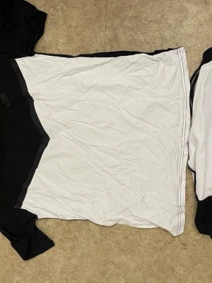 Nike svartvit t-shirt med logga - Snygg svartvit t-shirt från Nike med klassisk logga på bröstet. T-shirten har korta ärmar och är tillverkad i mjuk bomull. Den har en cool diagonal färgdelning mellan svart och vitt, vilket ger en sportig vibe.