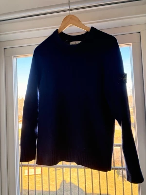 Mörkblå stickad tröja Stone Island - Säljer en mörkblå stickad tröja från Stone Island med klassisk patch på vänster ärm. Tröjan har rund halsringning, långa ärmar och ribbade muddar. Perfekt för dig som gillar stilrena och tidlösa plagg. Tröjan är i storlek M men skulle säga att den även passar folk som har S. Tröjans skick är grymt då jag bara använt den 2-3 gånger. Tveka inte på att höra av er vid frågor!😁🤩