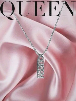 Silverfärgat halsband med QUEEN-hänge - Stilrent halsband i silverfärg med ett rektangulärt hänge där ordet QUEEN är täckt av gnistrande stenar. Perfekt för dig som vill sticka ut och visa att du är en queen. Kedjan är tunn och elegant, och hänget har en modern design.