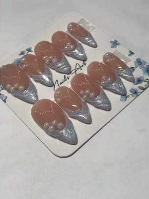 Press-on naglar blå chrome och pärlor  - Snygga press-on naglar i mandelform med nude bas och chrome blå spetsar. Dekorerade med små vita pärlor för en extra lyxig känsla. Perfekta för dig som vill ha trendiga och glamorösa naglar snabbt. Det följer med preppkit och limm vid köp av naglar 