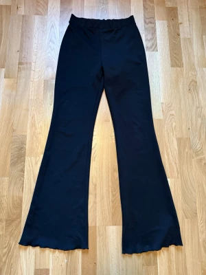 Svarta utsvängda leggings - Säljer ett par svarta leggings med utsvängda ben och vågig kant längst ner. De har hög midja och har även ett skönt material och sitter bekvämt.