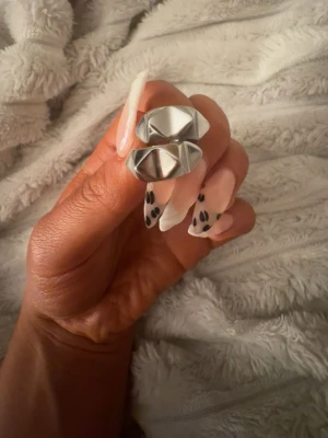 Silvriga geometriska örhängen - Säljer ett par örhängen i silverfärgad metall med en cool, geometrisk och kantig design. De har en modern look och reflekterar ljuset snyggt. Perfekta för dig som gillar statement-accessoarer och vill ha något unikt till din stil.