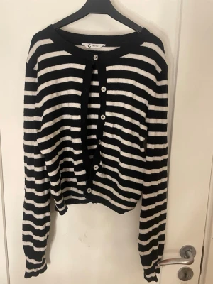 Randig svartvit kofta från Cubus - Säljer en svartvit randig kofta från Cubus med rund halsringning och vita knappar framtill. Koftan har långa ärmar och ribbade muddar vid ärmslut och nederkant. 