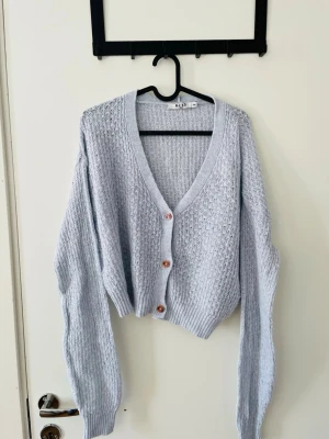 Ljusblå stickad kofta från NA-KD - Säljer en ljusblå stickad kofta från NA-KD med v-ringning och tre knappar framtill. Koftan har en croppad passform, långa ärmar och ribbade muddar. Stl känns mer som S.