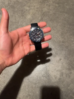 Ulysse Nardin svart klocka - Snygg klocka från Ulysse Nardin med svart urtavla och svart armband. Klockan har flera små urtavlor, silverfärgade detaljer och robust boett. 
