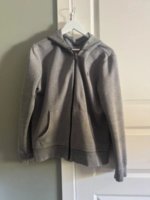 Grå zip-hoodie från Polo Ralph Lauren - Snygg grå hoodie med dragkedja från Polo Ralph Lauren. Klassisk modell med huva, två fickor framtill och diskret logga på bröstet. Perfekt för en chill och stilren look. Mjuk bomullsblandning som är skön att ha på sig hela dagen.