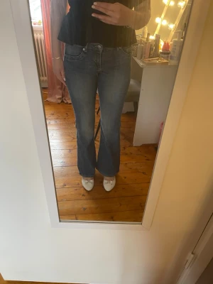 Blå bootcut jeans med mellanhög midja - Säljer ett par klassiska blå bootcut jeans med mellanhög midja och femficksmodell. Jeansen har en lätt tvättad look och är tillverkade i denim med lite stretch för skön passform. Perfekta till sneakers eller klackar.