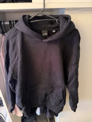 Svart hoodie från Only & Sons - En klassisk svart hoodie från Only & Sons med huva och stor magficka framtill. Hoodien har ribbade muddar vid ärmslut och nederkant. Perfekt för en avslappnad och stilren look. Materialet är mjukt och bekvämt, troligtvis bomullsblandning.