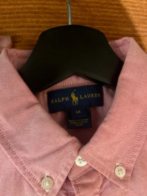 Rosa skjorta från Ralph Lauren - Klassisk rosa skjorta från Ralph Lauren  med button-down krage och vita knappar. Skjortan har lång ärm och är tillverkad i ett mjukt bomullstyg. Perfekt för sommaren. Pris kan diskuteras original pris 1500 