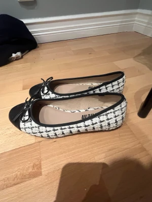 Svarta och vita ballerinaskor från Shein - Säljer ett par ballerinaskor från Shein i svart och vitt med rutigt tweedmönster. Skorna har svarta tåpartier i konstläder och en liten rosett framtill. Klassisk rundad tå och låg sula. Perfekta för en chic och trendig look.