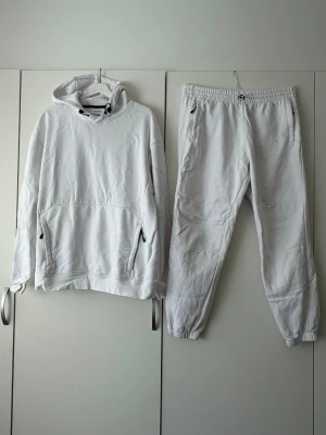 Vit loungewear-set med hoodie - Mysigt loungewear-set från Weekday i helvitt. Setet består av en hoodie med känguruficka och dragsko samt matchande mjukisbyxor med resår i midja och benslut. Perfekt för chill dagar hemma. Materialet är mjukt och bekvämt bomullstyg.