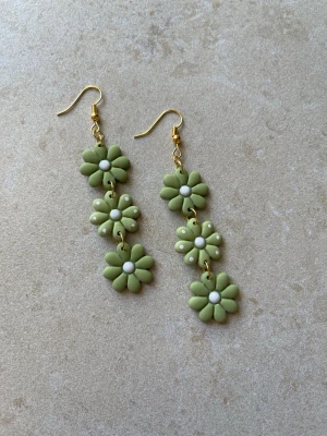 Handgjorda statementörhängen i grönt – blomdesign - Handgjorda statementörhängen i polymerlera  Varje blomma är formad för hand vilket gör att varje par är unikt och kan variera något i detaljer.  Ca 8 cm långa – tydliga men fortfarande lätta att bära.  Antiallergiska detaljer Lätta trots storleken Guldfärgade detaljer Flera par finns  Skriv om du vill se exakt par innan köp  Skickas