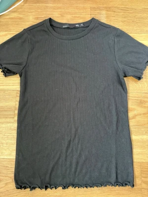 Svart ribbad t-shirt från 157 (3 stycken ) - Svart ribbad t-shirt från 157 i storlek XS. T-shirten har korta ärmar, rund halsringning och vågiga kanter vid ärmslut och nederkant. Perfekt för en chill och stilren look.