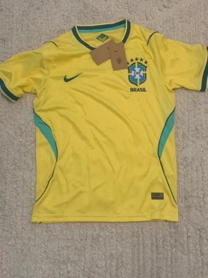 Brasilien Nike fotbollströja gul - HAR STORLEK S OCH M.             Snygg gul Brasilien fotbollströja från Nike med gröna detaljer och CBF-emblem på bröstet. Tröjan har korta ärmar, rund hals och är tillverkad i ett lätt och ventilerande material. Perfekt för fotbollsträning eller att bära när du hejar på landslaget. 