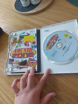 Arcade Zone till Nintendo Wii - Arcade Zone till Nintendo Wii är ett färgglatt och roligt spel där du kan spela klassiska arkadspel som Freeway, Megamania och Kaboom! Omslaget är vitt med färgglada illustrationer och spelet kommer i ett plastfodral. Perfekt för dig som gillar retrospel och partyspel.