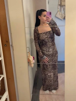 Lång leopardmönstrad klänning - Trendig långklänning med leopardmönster och fyrkantig ringning. Klänningen har långa ärmar och är tillverkad i ett tunt, lätt material som ger en snygg och smickrande passform. Perfekt för dig som vill sticka ut med en djärv look.