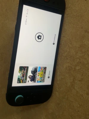 Nintendo Switch spelkonsol - Nintendo Switch spelkonsol med svart plastchassi och avtagbara Joy-Con-kontroller. Konsolen har en stor skärm och flera populära spel visas på displayen, bland annat Rocket League och Super Mario Party. En röd spelkassett medföljer.