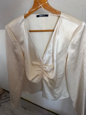 Champagnefärgad satintopp Gina Tricot - Snygg champagnefärgad blus från Gina Tricot i glansigt satintyg. Dragkedja på ena sidan, och ärmarna är skurna, se bild. använd fåtal gånger, dock finns där en söm som gått upp ( se bild) men som går att sy ihop! Obs liten i stl vid större byst 