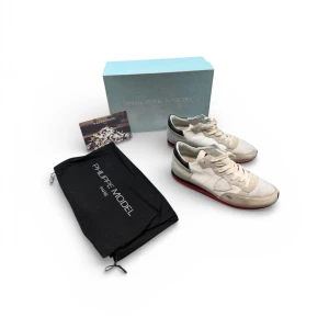 Philippe Model vita sneakers med röd sula - Snygga vita sneakers från Philippe Model med detaljer i mocka och läder, samt röd och svart rand på sulan. Klassisk låg modell med vita skosnören och diskret logga på sidan. Endast använda av mig fåtal gånger, jag har köpt dom nya med nypriset som ligger på 3400