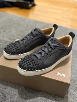 Christian Louboutin grå  - Gråa fräscha skor i mocka från Christian Louboutin med röd slät sula undertill och med svarta spikar. Perfekt för dig som vill ha en fräsch och stilig look till sommaren. Lite använda men fortfarande i mycket bra skick. Jag säljer dom pågrund av att jag har växt ur dom. Pris kan diskuteras hör av er vid intresse. Skokartong följer med