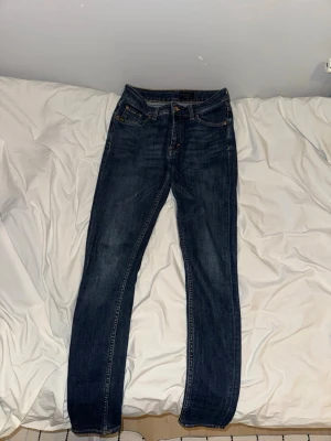 Mörkblå Jeans - Tiger Of Sweden - Snygga mörkblå skinny jeans från Lee med klassisk femficksdesign och guldfärgade sömmar. Jeansen har en smal passform och är tillverkade i stretchigt denimtyg för extra komfort. Perfekta till en avslappnad streetstyle-look.