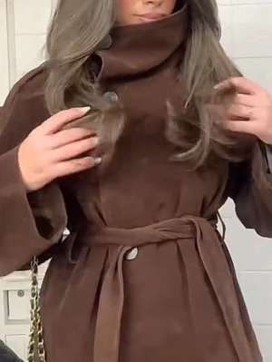 Brun kappa slutsåld från Gina  - Stilren brun kappa med hög krage och stora knappar framtill. Kappan har ett matchande knytband i midjan och vida ärmar. Perfekt för dig som vill ha en klassisk och trendig look. Materialet ser ut att vara mjukt och ger en lyxig känsla. Prislapp kvar