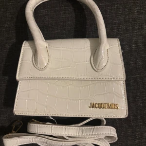 Vit handväska  - Vit handväska från Jacquemus med croco-mönstrad yta och guldfärgad logga framtill. Väskan är smutsig där bak men inget man lägger märke till. 