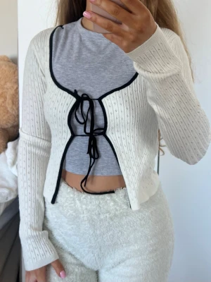 Kofta - Söt vit ribbad kofta med svarta kontrastkanter och knytband framtill. Koftan har lång ärm, croppad passform. Storlek XS från FB Sister (New Yorker) endast använd nån enstaka gång 💕