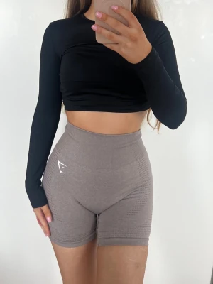Gymshark Shorts - Säljer ett par bruna/gråa högmidjade shorts från Gymshark. De är tighta och har en seamless design med diskret mönster på sidorna och logga framtill. Lappen är bortklippt men uppskattas vara storlek XS/S. Färgen är mest lik den första bilden 🤎