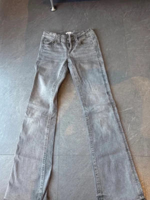 Grå bootcut jeans med fickdetaljer - Snygga grå bootcut jeans med klassisk femficksdesign och lock på bakfickorna. Jeansen har normalhög midja och är tillverkade i ett mjukt denimtyg. Perfekta för dig som gillar en avslappnad men trendig look. Är i tall 