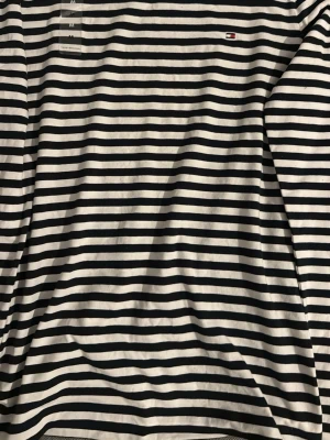 Randig långärmad topp Tommy Hilfiger - Snygg långärmad topp från Tommy Hilfiger i svart och vitt randigt mönster. Tillverkad i mjuk bomull med klassisk passform och diskret logga på bröstet. Perfekt för en stilren och avslappnad look.helt ny