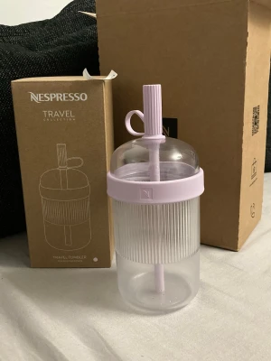 Nespresso Travel Tumbler lila plast - Obs kolla sista bilderna för att se defekt, ytan har blivit stäv/grainy. Säljer en Nespresso Travel Tumbler i genomskinlig och lila plast med räfflad yta och tillhörande sugrör. Perfekt för att ta med dryck på språng. Snygg och modern design från Nespresso Travel Collection. 