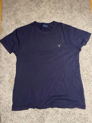 Mörkblå t-shirt från Gant - En stilren mörkblå t-shirt från Gant med diskret logga på bröstet. Klassisk rund halsringning och korta ärmar. Perfekt basplagg för en enkel och clean look.