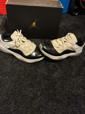 Air Jordan 11 Low svart/vit - Säljer ett par Air Jordan 11 Low sneakers i svart och vitt med klassisk Jumpman-logga på plösen. Skorna har en kombination av läder och textil på ovandelen samt en vit sula med genomskinliga detaljer. Perfekta för dig som gillar streetwear och sportig stil.