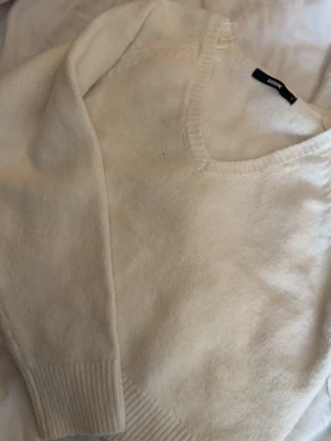 Vit stickad tröja från Bik Bok - Mysig vit stickad tröja från Bik Bok med v-ringning och långa ärmar. Tröjan har ribbade muddar vid ärmslut och nederkant. Perfekt för lager på lager och enkel att matcha med olika outfits.