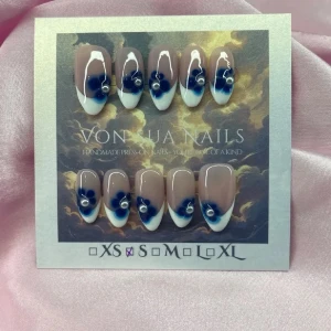 Sthlm (S);Medium Almond - Snygga handgjorda press-on naglar i en medium lånh mandelform . Designen har en nude bas, vit fransk tipp och handmålade blåa blommor med vita pärl detaljer. Perfekt för dig som vill ha en unik och trendig look. S: 15 mm, 11,5 mm, 12 mm, 11 mm, 9 mm 