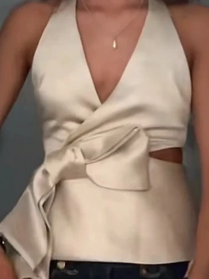 Champagnefärgad omlottopp med knyt - Snygg champagnefärgad omlottopp i satin med djup v-ringning och bred knytrosett i midjan. Toppen är ärmlös och har en elegant, figurnära passform som ger en lyxig känsla. Perfekt för dig som vill sticka ut med stilrena detaljer.