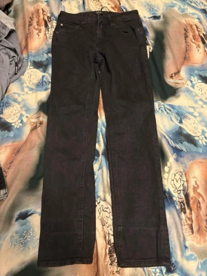 Svarta jeans från Jack & Jones - Säljer ett par svarta jeans från Jack & Jones med klassisk femficksdesign och raka ben. Jeansen har bälteshällor och knappgylf. Perfekta för dig som gillar en stilren och enkel look.