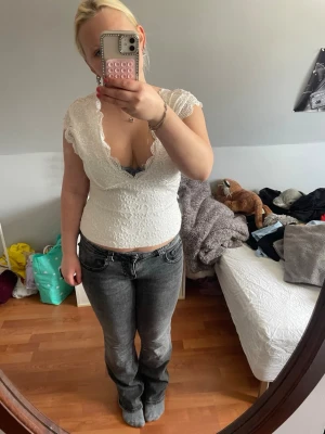 Vit spetsblus med öppen rygg - Säljer en vit, figurnära blus i spets med v-ringning och korta ärmar. Toppen har en snygg öppen rygg och fina spetsdetaljer längs kanterna. Perfekt för dig som gillar romantisk och feminin stil.