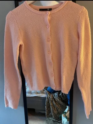 Ljusrosa kofta från 157 XS - Söt ljusrosa kofta från 157 i storlek XS. Koftan har rund halsringning, knappar framtill och är gjord i ett mjukt, fluffigt material som känns riktigt cozy. Perfekt att slänga på sig när det är lite kyligt ute.