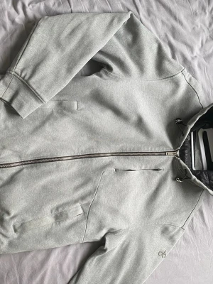 Ljusgrå hoodie från Moose Knuckles - Snygg ljusgrå hoodie från Moose Knuckles med dragkedja framtill, fickor på sidorna och en bröstficka. Stor Moose-logga i svart på ryggen och liten logga på ärmen. Huva med dragsko och mjukt material som känns riktigt skönt. Perfekt för en avslappnad streetwear-look. Nypris 5799kr och digitalkvitto finns. Bara att skriva vid frågor och priset går såklart att diskutera!